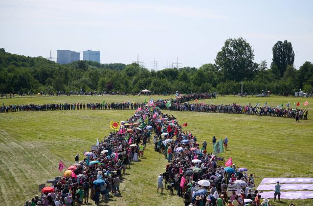 30 May 2026, North Rhine-Westphalia, Hamm: Demonstrators form a wind turbine against the backdrop of a power plant. A climate alliance consisting of Fridays for Future, Greenpeace, BUND and Campact has called for the rally under the motto "Future instead of gas - defending the energy transition". Photo: Bernd Thissen/dpa