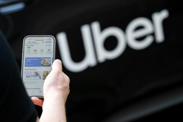 FILED - 08 August 2024, Berlin: FILE PHOTO - A man holds his smartphone in front of a rental car with a sign from the mobility service provider and ride broker Uber. Photo: Sebastian Gollnow/dpa
