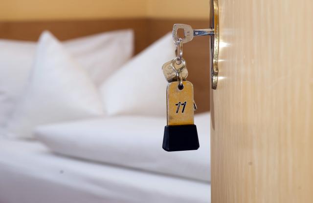 FILED - 27 November 2014, Lower Saxony, Goslar: A room key is hanging in the door lock in front of a bed at a guesthouse. Photo: Swen Pförtner/dpa