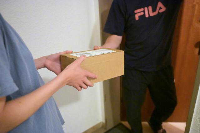 FILED - 19 May 2026, Bavaria, Munich: FILE PHOTO - In a hallway, a resident hands a parcel to a neighbor (re-enacted scene). Photo: Malin Wunderlich/dpa