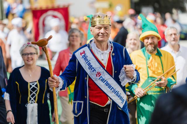 07 June 2026, Thuringia, Suhl: The reigning Thuringian Bratwurst King Norbert I (C, Norbert Abt) walks alongside fellow product royalty and traditional figures during a parade through the city center of Erfurt, Germany. Later today, Norbert seeks to defend his crown alongside his "Suhler Grillzwerge" teammates to secure his 10th title at the annual bratwurst grilling championship. Photo: Michael Reichel/dpa