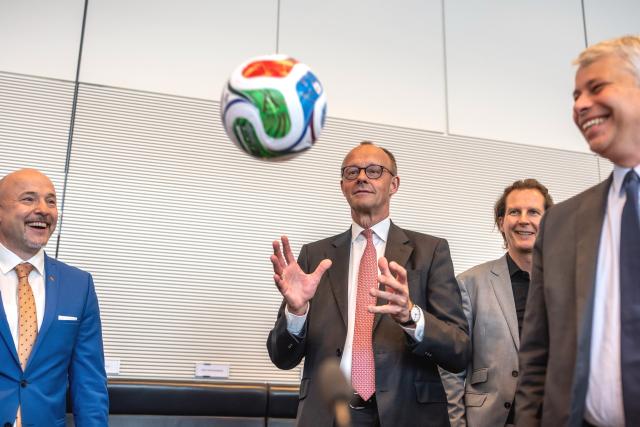 09 June 2026, Berlin: Friedrich Merz (C), Germany's Chancellor, catches a soccer ball before the start of the parliamentary group meeting in the German Bundestag. Photo: Michael Kappeler/dpa