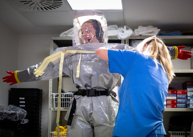 09 June 2026, Berlin: Louise Goetze (L), intensive care nurse and coordinator in the special isolation ward at Charite, is dressed in a gray protective suit with the help of a colleague during a press event. Photo: Soeren Stache/dpa