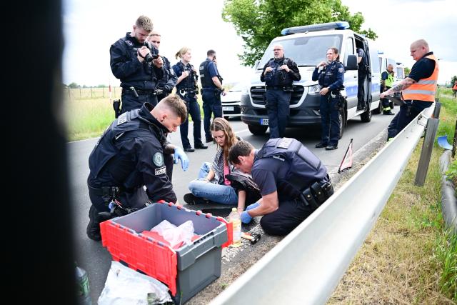 10 June 2026, Berlin, Berlin-Schönefeld: Law enforcement officers work to detach and remove a demonstrator who blocked an access road leading to the Berlin ExpoCenter Airport. Photo: Sebastian Christoph Gollnow/dpa