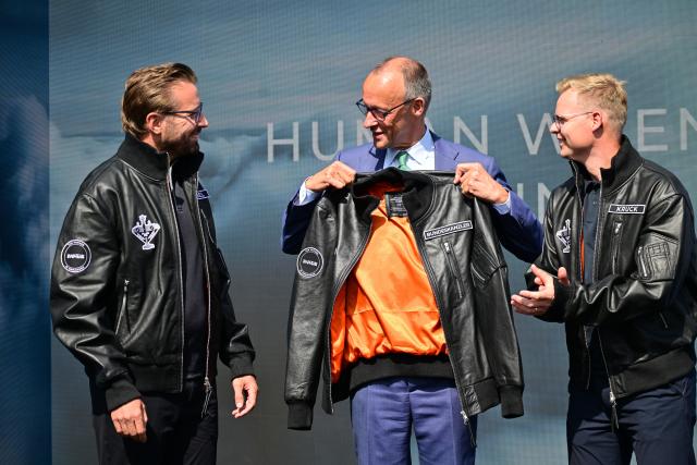 SYMBOL - 10 June 2026, Brandenburg, Schoenefeld: Friedrich Merz (C), German Chancellor, looks at a jacket he received from Quantum-Systems during a tour of the International Aerospace Exhibition (ILA). Photo: Sebastian Gollnow/dpa