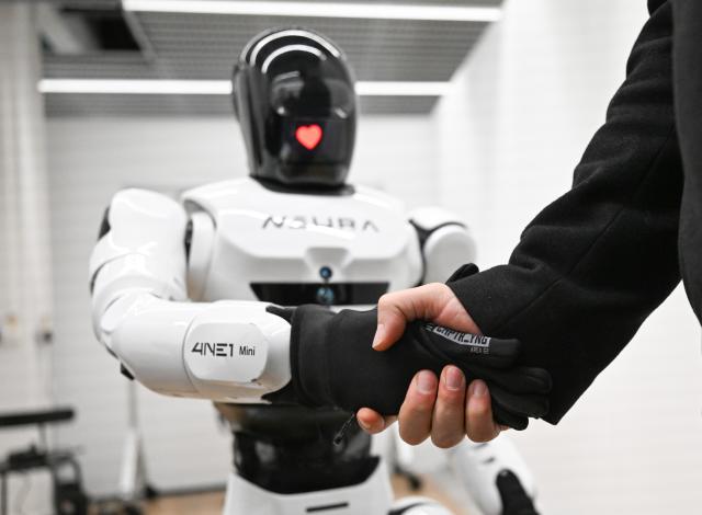FILED - 02 February 2026, Baden-Wuerttemberg, Metzingen: FILE PHOTO - David Reger, the founder and CEO of Neura Robotics, shakes hands with a humanoid robot. Photo: Bernd Weißbrod/dpa
