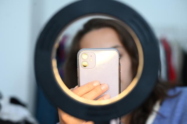 ILLUSTRATION - 05 July 2024, Berlin: FILE PHOTO - A woman takes photos behind a ring light. The German health insurer DAK-Gesundheit and the University Medical Center Hamburg-Eppendorf (UKE) analysis found that nearly half of 10- to 17-year-olds discover products through social media advertising, while 40 percent are influenced by recommendations from online influencers. Photo: Niklas Graeber/dpa