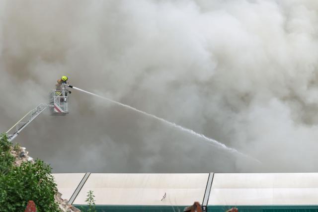 16 June 2026, Bavaria, Dettelbach: Firefighters are using a turntable ladder to extinguish a fire in a pile of scrap tires and cables on the grounds of a waste disposal company. Authorities are warning residents due to heavy smoke. Photo: Daniel Löb/dpa