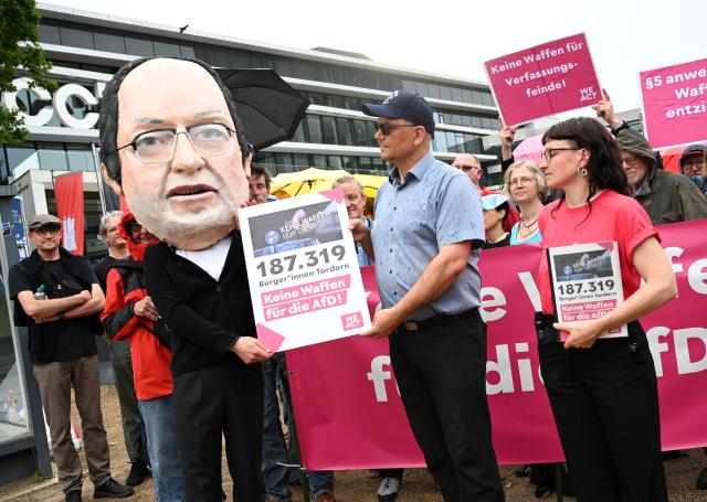 17 June 2026, Hamburg: Thomas Guenther, the founder of an initiative to ban weapons for the Alternative for Germany (AfD) members, symbolically presents signatures to a man dressed as German Interior Minister Alexander Dobrindt alongside Lara, a campaigner for WeAct, during a protest on the sidelines of the 2026 Conference of Interior Ministers. Photo: Daniel Bockwoldt/dpa