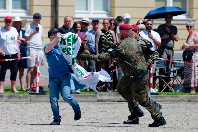 18 June 2026, Baden-Wuerttemberg, Karlsruhe: A protester is being detained by military police as soldiers march into the Schlossplatz for the ceremonial oath-taking of more than 350 recruits. Photo: Uwe Anspach/dpa