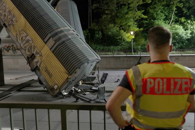 20 June 2026, Bavaria, Munich: Apolice officer looks at two freight-train cars lying on a road after they fell off a bridge in Munich. Photo: Ehsan Monajati/dpa