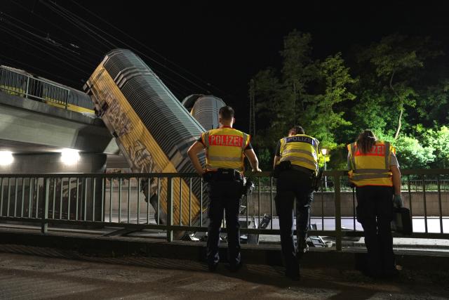 20 June 2026, Bavaria, Munich: Police officers look at two freight-train cars lying on a road after they fell off a bridge in Munich. Photo: Ehsan Monajati/dpa