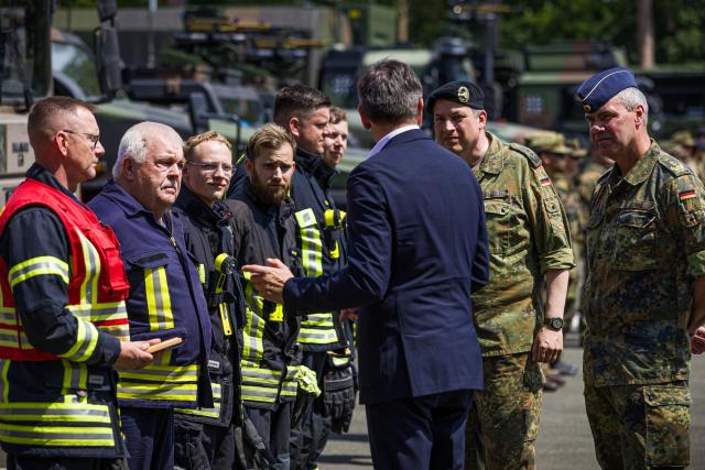 20 June 2026, Lower Saxony, Nienburg (Weser): Olaf Lies (C), Minister President of Lower Saxony, speaks with firefighters during the multinational NATO exercise "CIMIG Quadriga 2026" at the Clausewitz Barracks. The exercise will take place from June 14 to 26, 2026. Under the leadership of the German Armed Forces (Bundeswehr), the exercise will test the coordination between military forces and civilian actors in crisis scenarios. Photo: Moritz Frankenberg/dpa