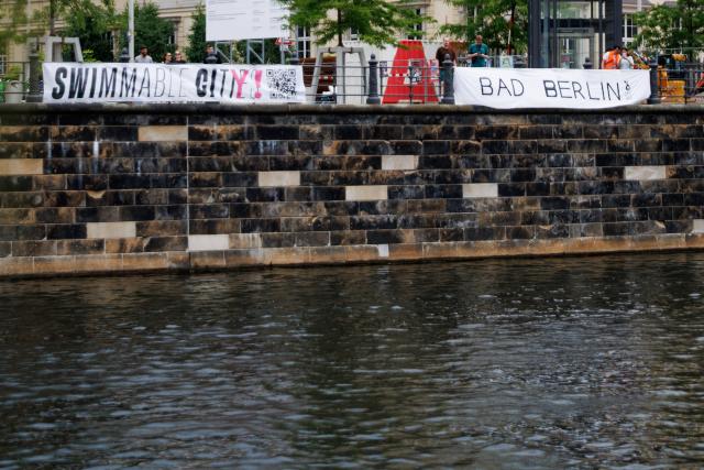 20 June 2026, Berlin: Two banners reading "Swimmable City!" and "Bad Berlin" are displayed on the banks of the Spree, during the swimming demonstration, held under the slogan "Vote to End 101 Years of the Swimming Ban!". The demonstration was held to protest the ban on swimming in the Spree. Photo: Carsten Koall/dpa