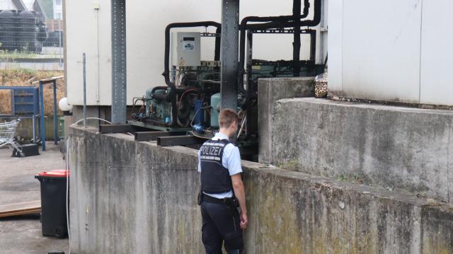 21 June 2026, Baden-Wuerttemberg, Hockenheim: A police officer inspects charred equipment near a conveyor belt at a kebab factory. According to a police spokesperson, the business owner and his son were able to escape unharmed. When firefighters arrived at the scene, a car and parts of the factory's equipment were engulfed in flames. Photo: Rene Priebe/dpa