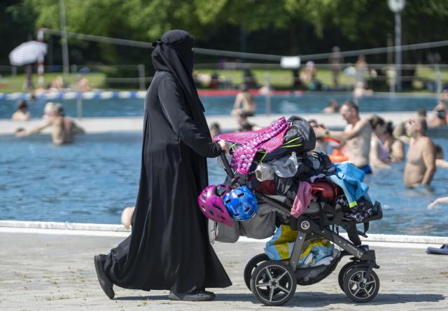 21 June 2026, Bavaria, Munich: A fully veiled woman pushes a stroller past a swimming pool at the Michaelibad. Summer-like heat is expected to continue over the next few days. Photo: Stefan Puchner/dpa