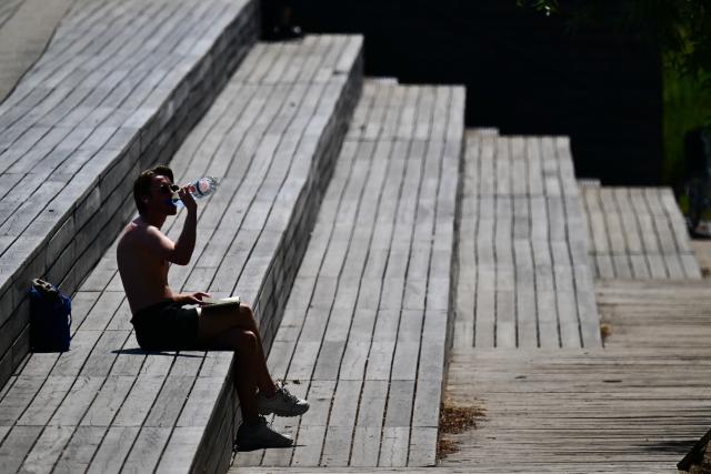 23 June 2026, Berlin: A man is sitting in the sun in the park at Gleisdreieck, drinking water. Photo: Sebastian Gollnow/dpa