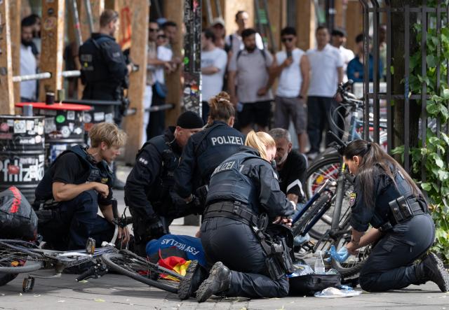 23 June 2026, Hesse, Frankfurt am Main: German police officers gather around an injured man near Frankfurt's Central train station. An unclear incident has prompted a large-scale deployment of police and emergency responders. Witnesses heard gunshots, and a man was subsequently treated while lying on the ground on the station forecourt, according to dpa reporters. Photo: Boris Roessler/dpa