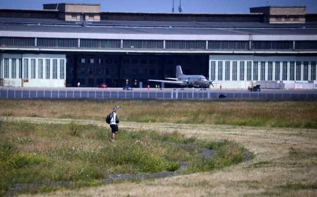 25 June 2026, Berlin: A person takes a selfie at Tempelhofer Feld in front of the former Tempelhof Airport terminal building, with an aircraft parked outside. Only a few pedestrians, skaters and cyclists are out on the field amid midsummer heat, as Berlin and Brandenburg brace for what could be the hottest days of the year, with the German Weather Service (DWD) forecasting temperatures of up to 40 degrees Celsius. Photo: Bernd von Jutrczenka/dpa - ACHTUNG: Nur zur redaktionellen Verwendung im Zusammenhang mit der aktuellen Berichterstattung und nur mit vollständiger Nennung des vorstehenden Credits