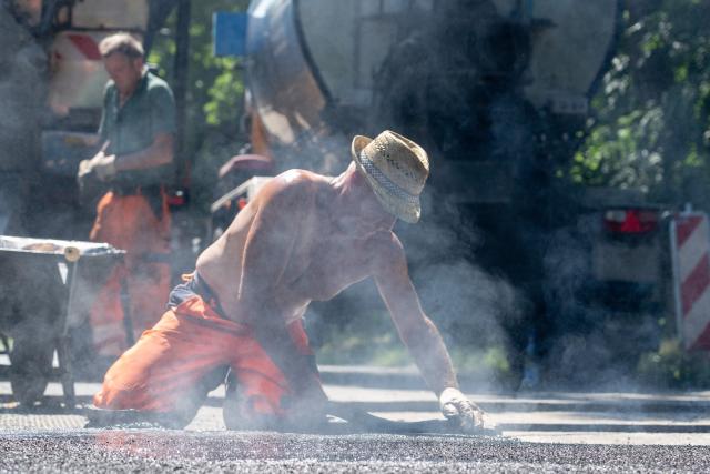 25 June 2026, Brandenburg, Potsdam: Asphalt workers pave a street with mastic asphalt heated to 210 degrees Celsius under the midday sun at 33 degrees Celsius. Photo: Georg Moritz/dpa