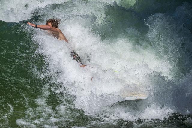 25 June 2026, Bavaria, Munich: A surfer plunges into the cool waters of the Eisbach Wave after riding its standing wave in the English Garden during the height of summer. A popular hotspot for surfers and tourists alike, it attracts visitors year-round, regardless of season or time of day. Photo: Peter Kneffel/dpa