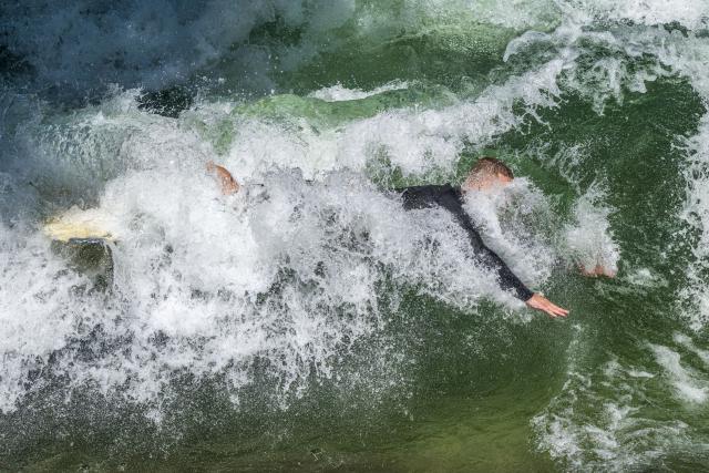 25 June 2026, Bavaria, Munich: A surfer plunges into the cool waters of the Eisbach Wave after riding its standing wave in the English Garden during the height of summer. A popular hotspot for surfers and tourists alike, it attracts visitors year-round, regardless of season or time of day. Photo: Peter Kneffel/dpa