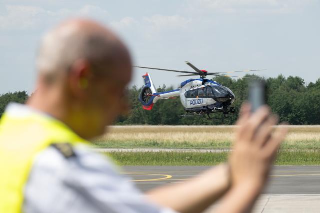 25 June 2026, Saxony, Dresden: A federal police officer watches as the new Airbus H145 police helicopter lands at Dresden Airport during the commissioning ceremony. The new helicopters are more powerful and larger than their predecessors. Photo: Sebastian Kahnert/dpa