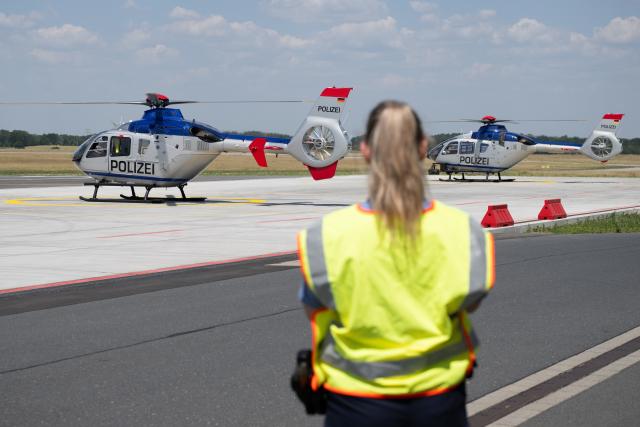25 June 2026, Saxony, Dresden: A federal police officer watches as the current fleet of Airbus EC135 police helicopters takes off from Dresden Airport. The occasion is the commissioning of three new police helicopters for the Saxony Police. Photo: Sebastian Kahnert/dpa