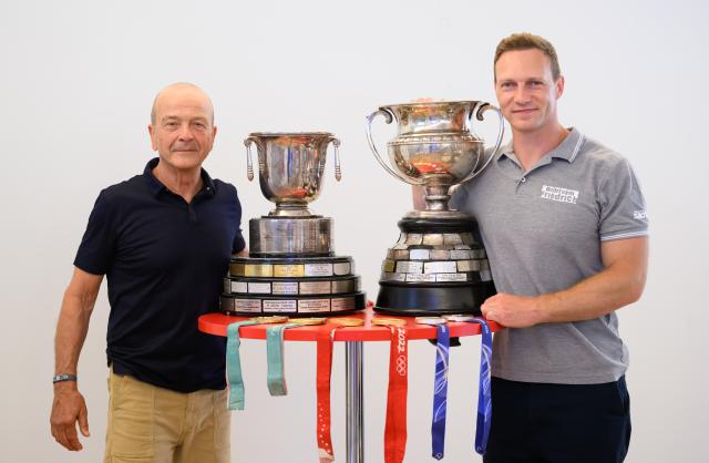 25 June 2026, Saxony, Dresden: German bobsled pilot Francesco Friedrich (R) and his coach Gerd Leopold stand at a table with the World Championship trophies and Olympic medals after a press conference. The world's most successful bobsled pilot will continue his bobsledding career through the 2030 Winter Olympics. Photo: Robert Michael/dpa