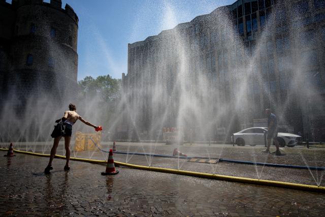 26 June 2026, North Rhine-Westphalia, Cologne: Passersby cool off at a water fountain installed on Rudolfplatz in downtown Cologne as part of the city's "Cooling Cologne" heat relief initiative. Photo: Henning Kaiser/dpa