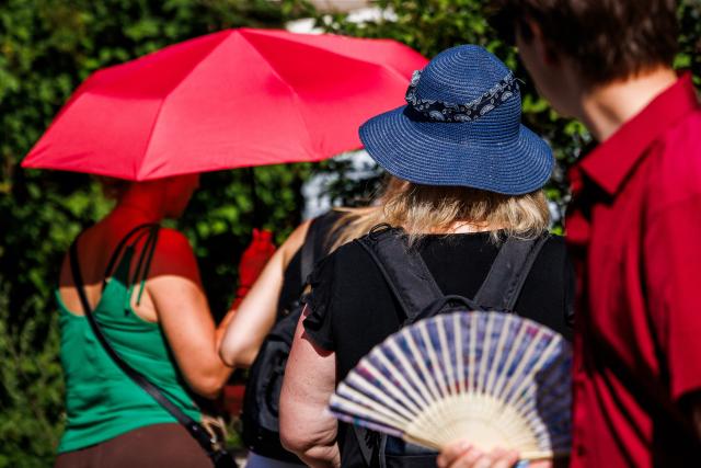 26 June 2026, Sieversdorf: Fans of American musician Bruno Mars wear hats, hold umbrellas and use handheld fans as they make their way to his concert at Berlin's Olympic Stadium. A heat wave is currently sweeping through Brandenburg and Berlin. Photo: Carsten Koall/dpa
