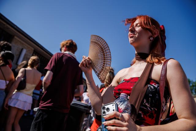 26 June 2026, Berlin: A young woman holds a fan to cool off on her way to a concert by American musician Bruno Mars at the Olympic Stadium. A heat wave is currently sweeping through Brandenburg and Berlin. Photo: Carsten Koall/dpa