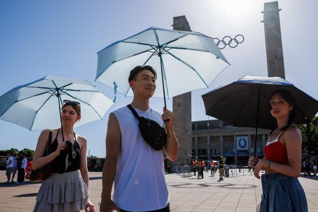 26 June 2026, Sieversdorf: Fans of Bruno Mars hold umbrellas as they make their way to his at Berlin's Olympic Stadium. A heat wave is currently sweeping through Brandenburg and Berlin. Photo: Carsten Koall/dpa