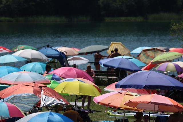 27 June 2026, Bavaria, Rosshaupten: People seek relief from the heat under beach umbrellas on the shore of Lake Illasberg, on the edge of the Alps, during hot summer weather. Photo: Karl-Josef Hildenbrand/dpa