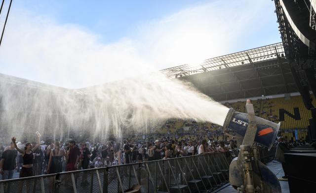 27 June 2026, Saxony, Dresden: Fans of the German band Kraftklub cool off under a water spray during a heatwave before the start of a concert at the 2026 "Sterben in Karl-Marx-Stadt" Open Air festival at Rudolf-Harbig Stadium. Photo: Robert Michael/dpa