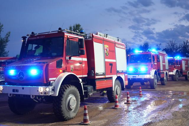 28 June 2026, Rhineland-Palatinate, Traisen: Fire department emergency vehicles are stationed near a nature reserve in the Bad Kreuznach district, where a wildfire has spread. The forest fire, which continues to spread in this area contaminated with unexploded ordnance, has led to the evacuation of the entire municipality of Traisen. Photo: Kevin Schößler/dpa