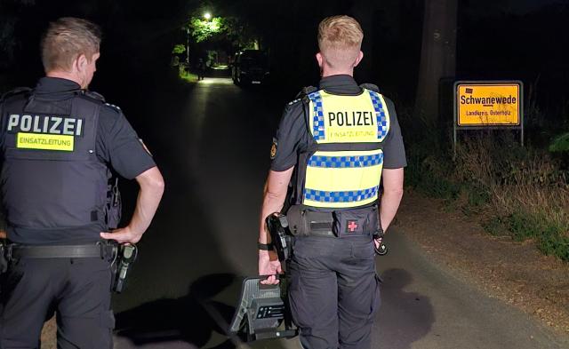 29 June 2026, Lower Saxony, Schwanewede: Two police officers stand at the entrance to Schwanewede with a portable floodlight. In the case of the couple killed in Bremen, the police have arrested the suspected perpetrator. Photo: Kai Moorschlatt/dpa