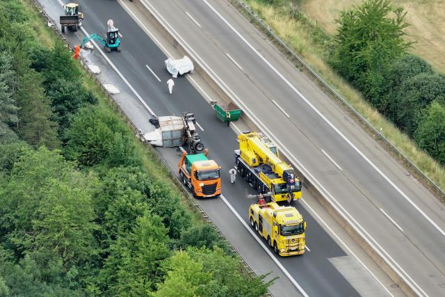 30 June 2026, North Rhine-Westphalia, Mechernich: An aerial drone view shows an overturned commercial truck lying across multiple traffic lanes on the A1 highway. Local police completely closed the heavily traveled transit route in both directions between the Mechernich and Nettersheim interchanges in the Euskirchen district following a hazardous materials accident involving spilled asbestos waste, triggering severe regional traffic disruptions. Photo: STR/dpa