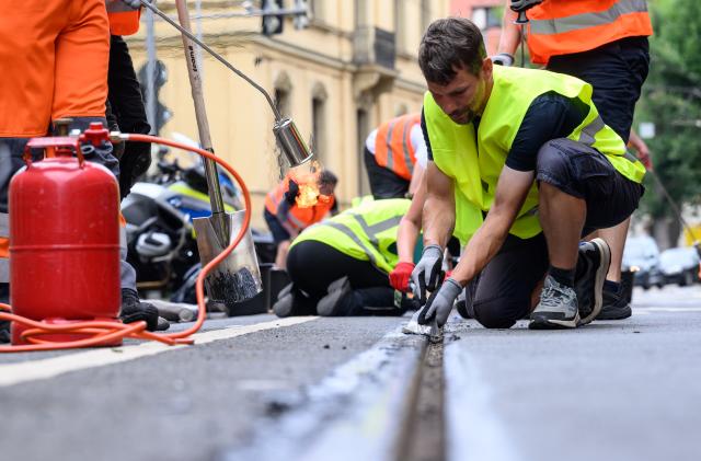 30 June 2026, Saxony, Leipzig: Volunteers, including Stefan Engwicht, scrape caked-on joint sealant from tram tracks in Leipzig city centre. Since 27 June 2026, virtually no trams have been running in the city due to heat damage to the tracks. The Leipzig Public Transportation Authority (LVB) has appealed to the public to help remove the oozed-out joint sealant. Photo: Hendrik Schmidt/dpa