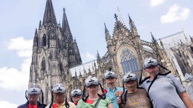 01 July 2026, North Rhine-Westphalia, Cologne: A group of tourists wearing VR headsets stands on Roncalliplatz in front of Cologne Cathedral. Using TimeRide, they experience a virtual glimpse of the cathedral's construction. From 1 July, admission to the cathedral costs visitors 12 euros. Worshippers continue to have free access to a designated area. Photo: Rolf Vennenbernd/dpa