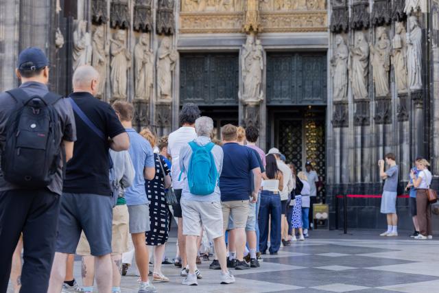 01 July 2026, North Rhine-Westphalia, Cologne: Tourists stand in front of the main entrance to Cologne Cathedral. From 1 July, admission to the cathedral costs visitors 12 euros. Those wishing to pray continue to have free access to a designated area. Photo: Rolf Vennenbernd/dpa