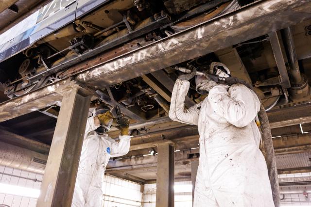 01 July 2026, Bavaria, Nuremberg: Employees at the VAG public transport company's maintenance workshop demonstrate the use of a dry-ice blasting machine to clean a tram's undercarriage contaminated with bitumen (staged scene). Nuremberg's trams have been out of service since the weekend due to heat-related damage. High temperatures cause the bitumen on the roads to soften, causing it to adhere to the tracks and the trams' undercarriages. Cleaning the trams is therefore labour-intensive, with dry ice being one of the methods used. Photo: Daniel Karmann/dpa