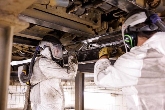 01 July 2026, Bavaria, Nuremberg: Employees at the VAG public transport company's maintenance workshop demonstrate the use of a dry-ice blasting machine to clean a tram's undercarriage contaminated with bitumen (staged scene). Nuremberg's trams have been out of service since the weekend due to heat-related damage. High temperatures cause the bitumen on the roads to soften, causing it to adhere to the tracks and the trams' undercarriages. Cleaning the trams is therefore labour-intensive, with dry ice being one of the methods used. Photo: Daniel Karmann/dpa