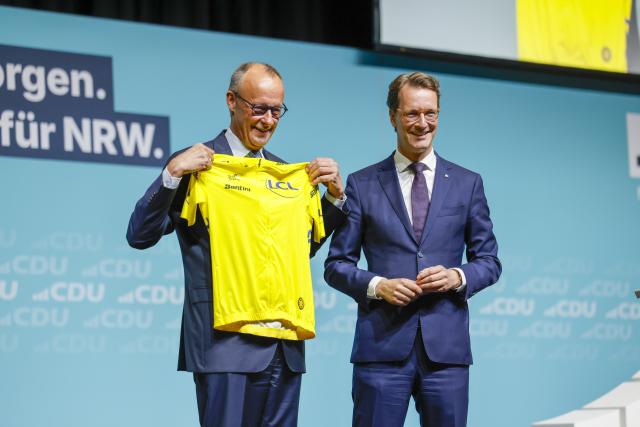 04 July 2026, North Rhine-Westphalia, Duesseldorf: Hendrik Wuest (R), Minister President of North Rhine-Westphalia, presents German Chancellor Friedrich Merz with a yellow road cycling jersey during the Christian Democratic Union (CDU) North Rhine-Westphalia state party convention. Photo: Thomas Banneyer/dpa