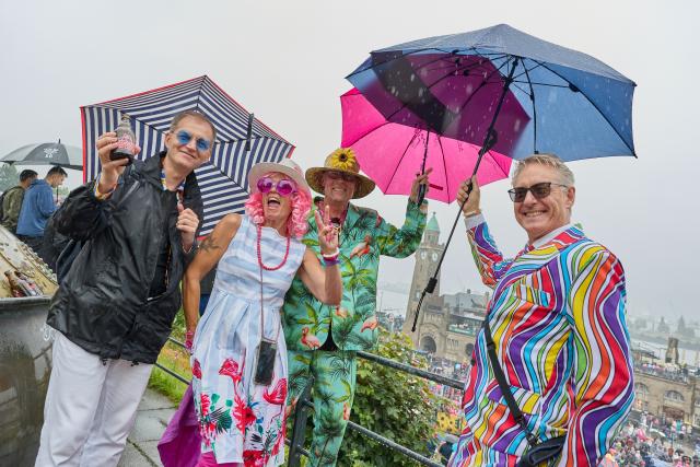 04 July 2026, Hamburg: Partiers holding colorful umbrellas stand in front of the Landungsbruecken during the 2026 Schlagermove parade. Photo: Georg Wendt/dpa