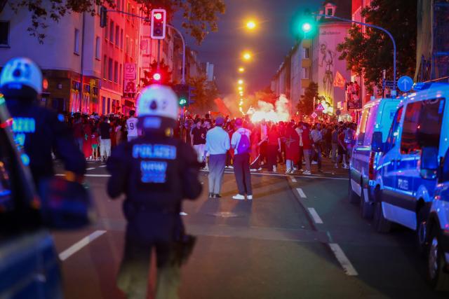04 July 2026, North Rhine-Westphalia, Duesseldorf: Bengal fires are lit as Moroccan soccer fans celebrate their victory over Canada in the World Cup round of 16. Police officers watch the crowd from a distance. Photo: Christoph Reichwein/dpa