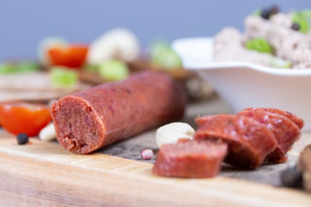 FILED - 06 January 2024, Saxony, Dresden: FILE PHOTO - Slices of bread topped with various vegan sausages, a vegan garlic sausage, and a bowl of a pea-based vegan liver sausage alternative, all arranged on a wooden board. Photo: Sebastian Kahnert/dpa