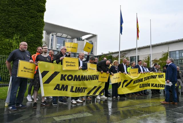 07 July 2026, Berlin: Mayors and finance directors stand in front of the Federal Chancellery holding signs that read "Municipalities at Their Limit" during a demonstration by cities and municipalities calling for more financial support from the federal government Under the slogan "For the Dignity of Our Cities". Photo: Jens Kalaene/dpa