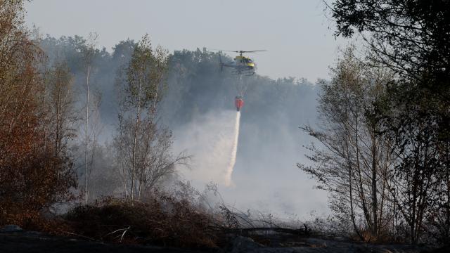 10 July 2026, Thuringia, Meuselwitz: A firefighting helicopter drops water over a forested area. The fire broke out at the end of June on a former open-pit mining site. Photo: Bodo Schackow/dpa