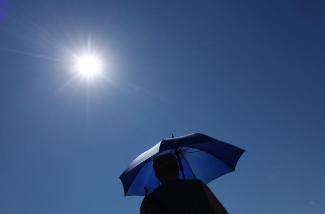 11 July 2026, Munich, Marktoberdorf: A woman walks under a parasol in the blazing sun during hot weather. Photo: Karl-Josef Hildenbrand/dpa